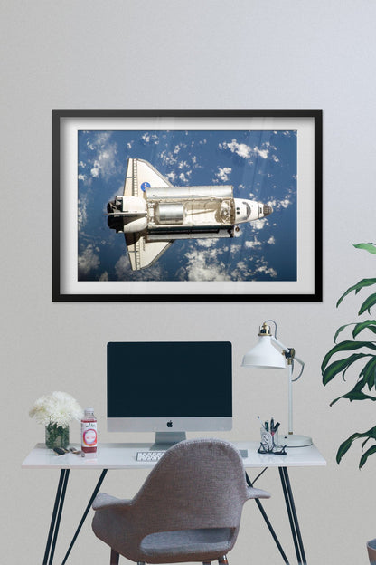 Space Shuttle Endeavour in orbit poster framed above a desk with a computer