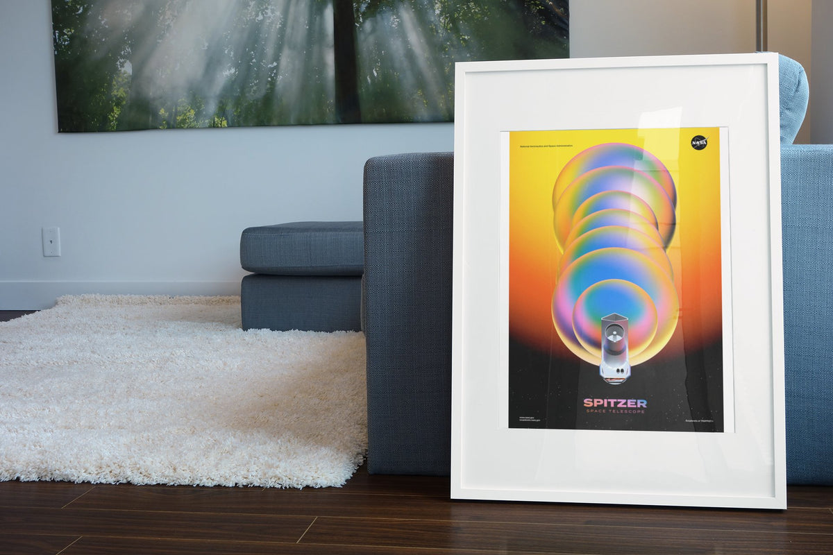 Spitzer Space Telescope poster in a white frame leaning beside a blue sofa