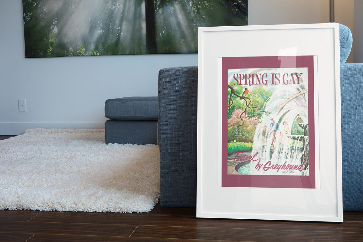 Spring is Gay Greyhound poster leaning beside a blue sofa