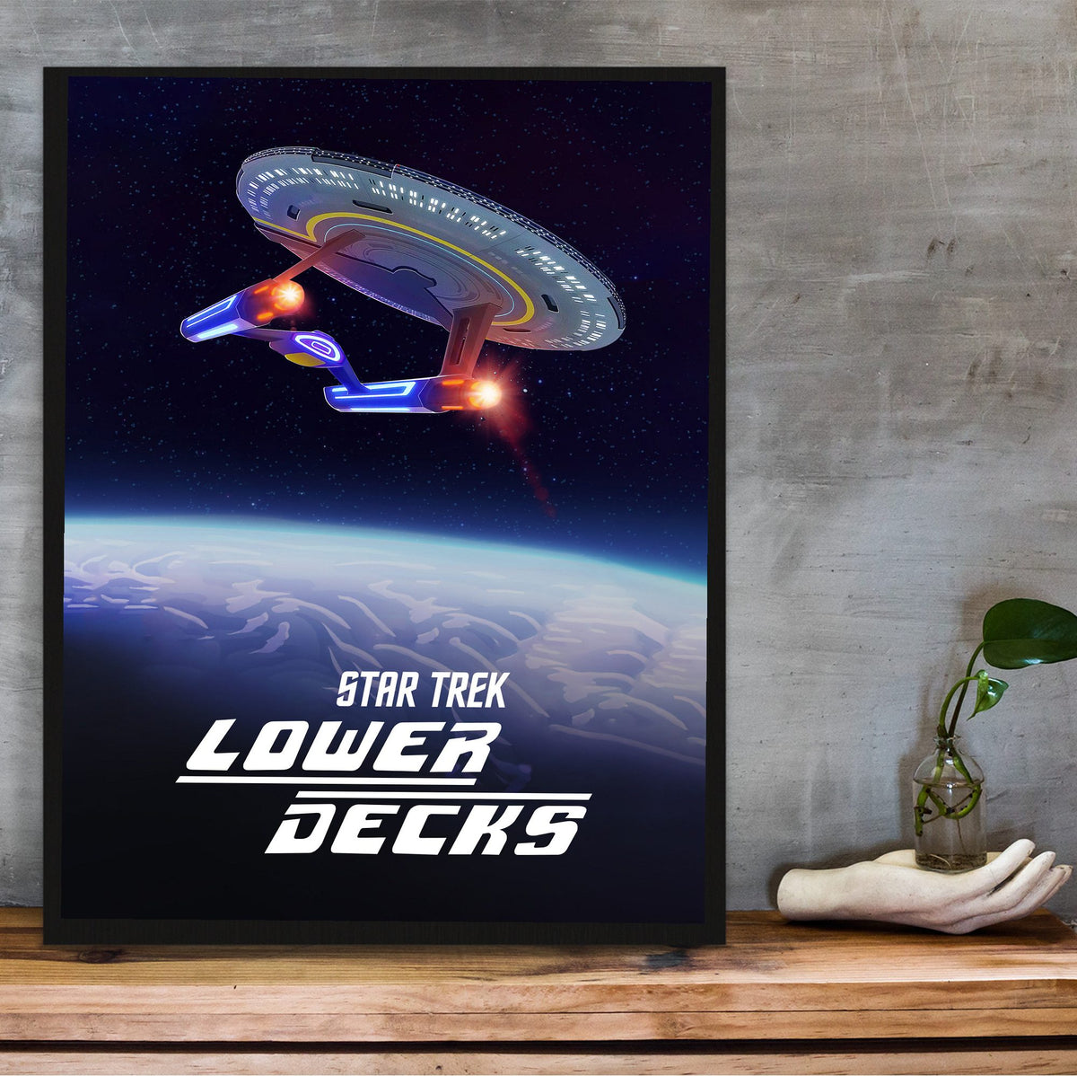 Star Trek: Lower Decks poster in a black frame on a wooden shelf against concrete