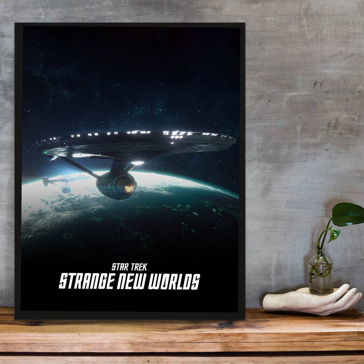 Star Trek: Strange New Worlds poster in a black frame on a wooden shelf against concrete