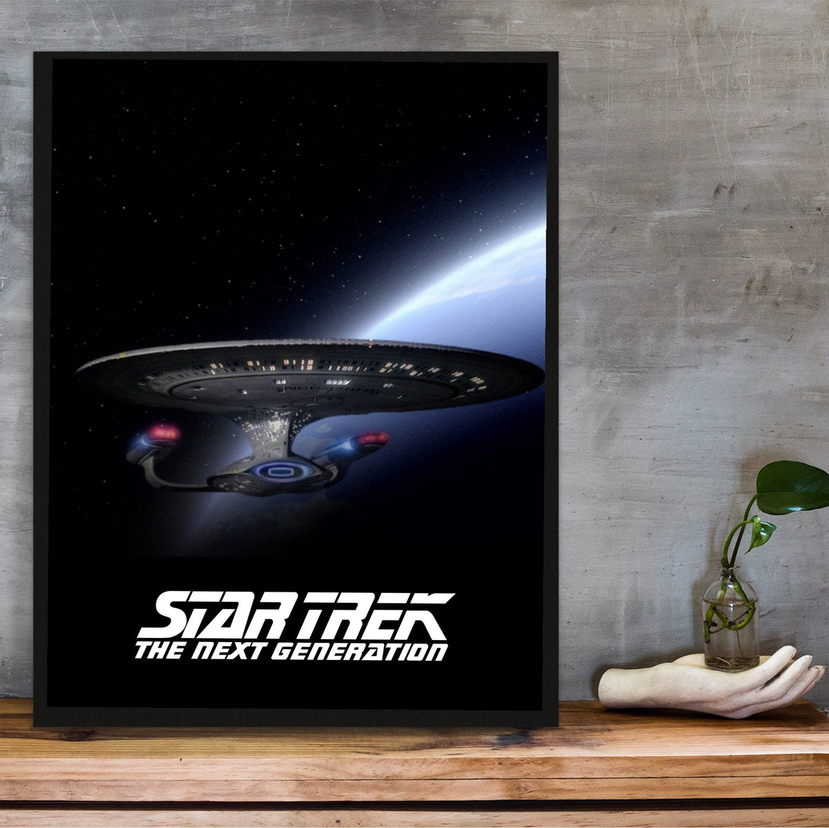 Star Trek: The Next Generation poster in a black frame on a wooden shelf against concrete