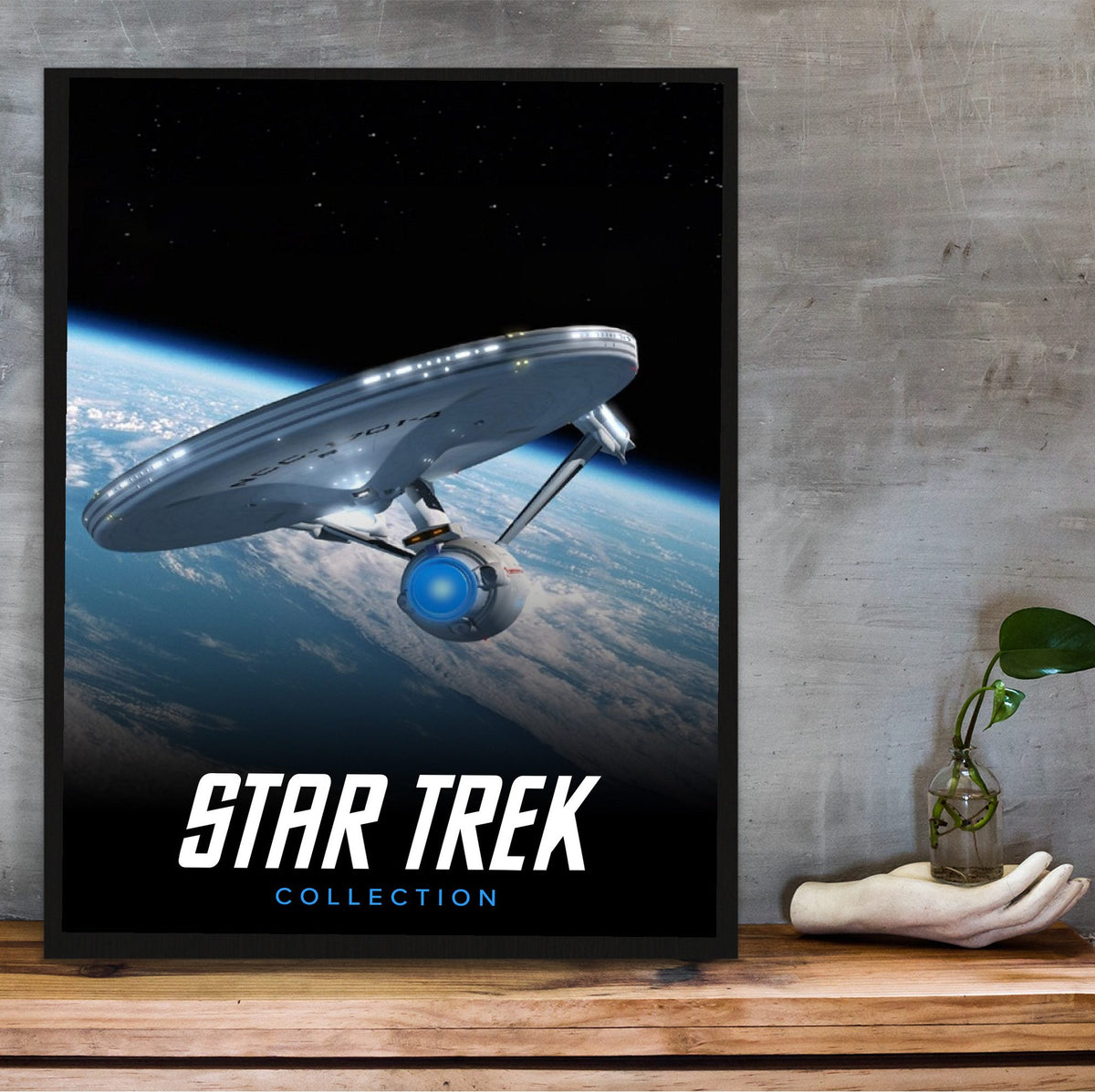 Star Trek TV Collection Art poster in a black frame on a wooden shelf against concrete