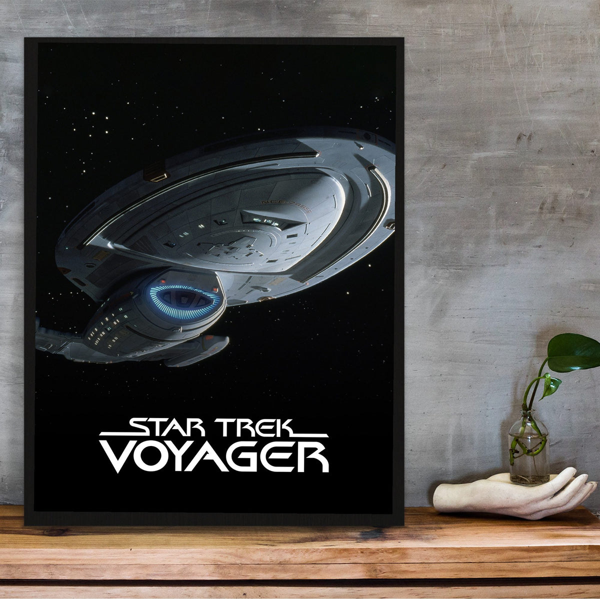 Star Trek: Voyager poster in a black frame on a wooden shelf against concrete