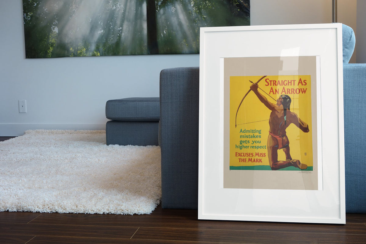 Straight as an Arrow poster in a white frame leaning beside a blue sofa