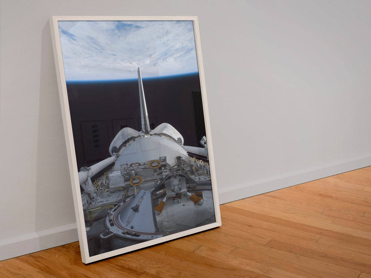 STS-123 Space Shuttle leaving the ISS poster in a white frame leaning against a wall