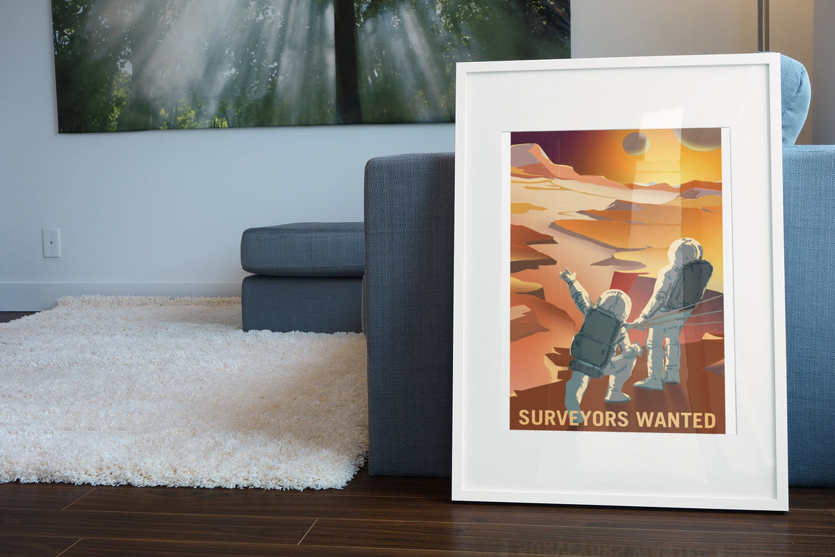 Surveyors Wanted on Mars poster in a white frame leaning beside a blue sofa