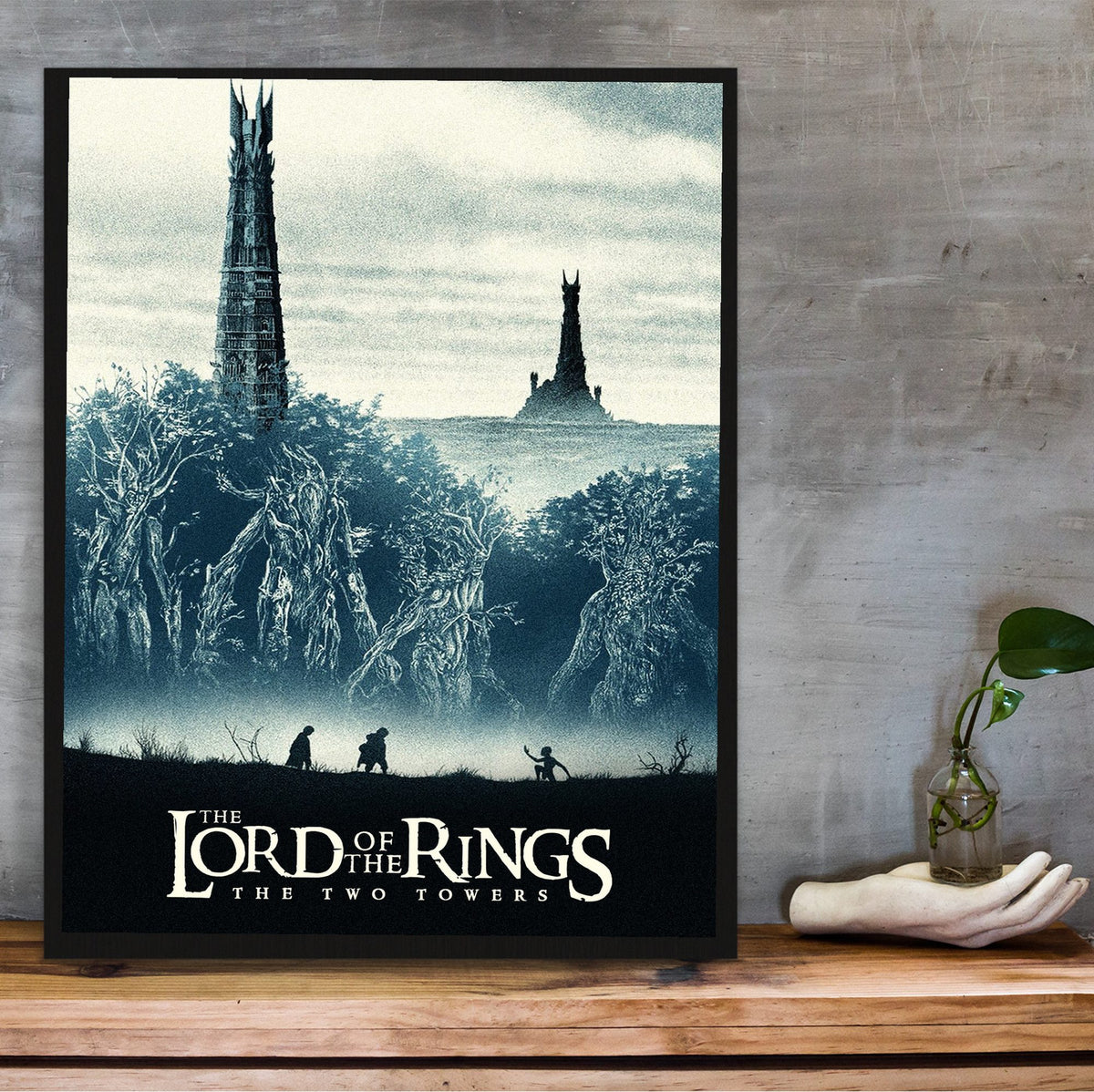 The Lord of the Rings: The Two Towers (2002) Movie Two Towers Art poster in a black frame on a wooden shelf against concrete