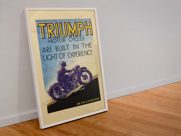 Triumph Motorcycles poster in a white frame leaning against a wall