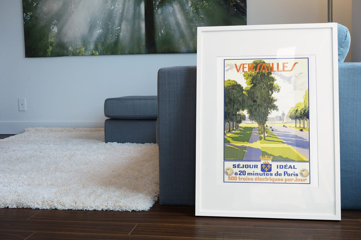 Versailles Sejour Ideal poster leaning beside a blue sofa