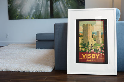 Visby — Town of Ruins and Roses poster leaning beside a blue sofa