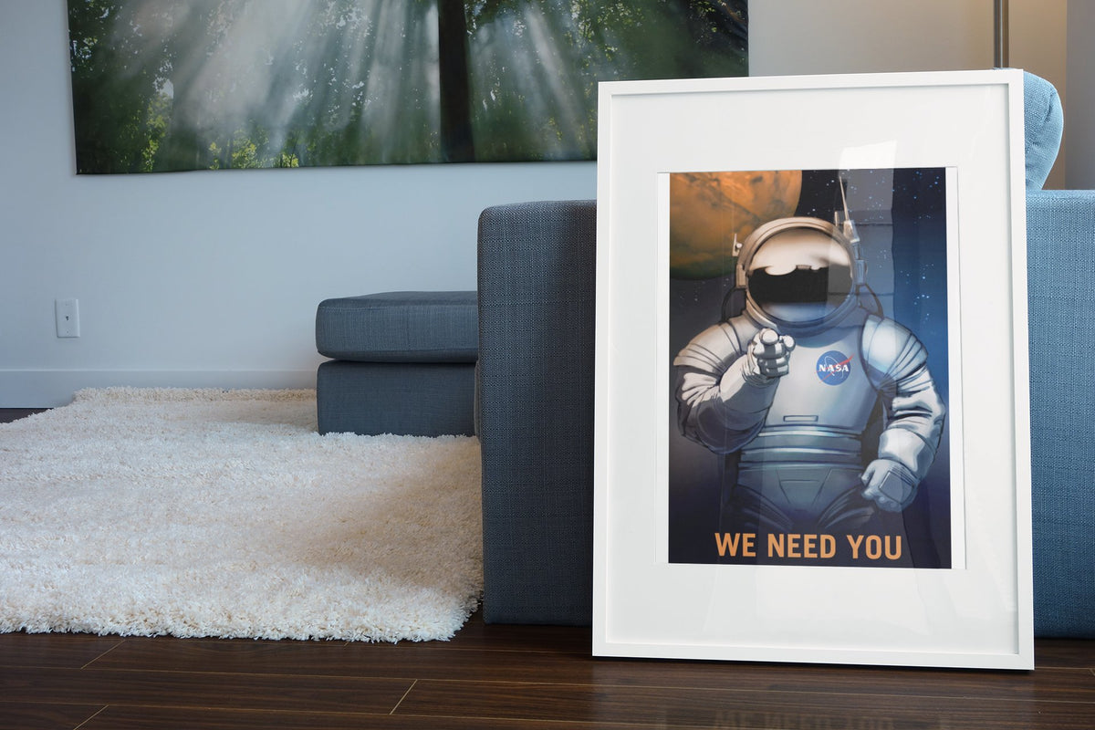 We Need You on Mars NASA recruitment poster in a white frame leaning beside a blue sofa