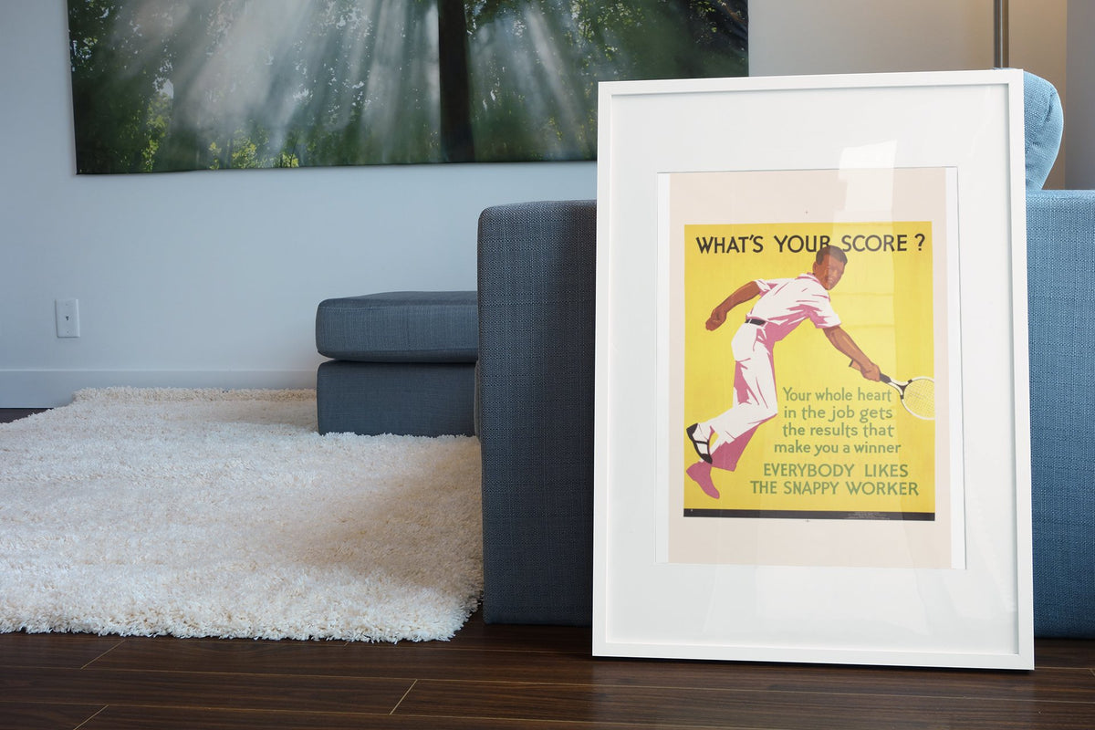 What’s Your Score poster in a white frame leaning beside a blue sofa