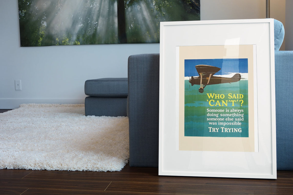 Who Said “Can’t” poster in a white frame leaning beside a blue sofa