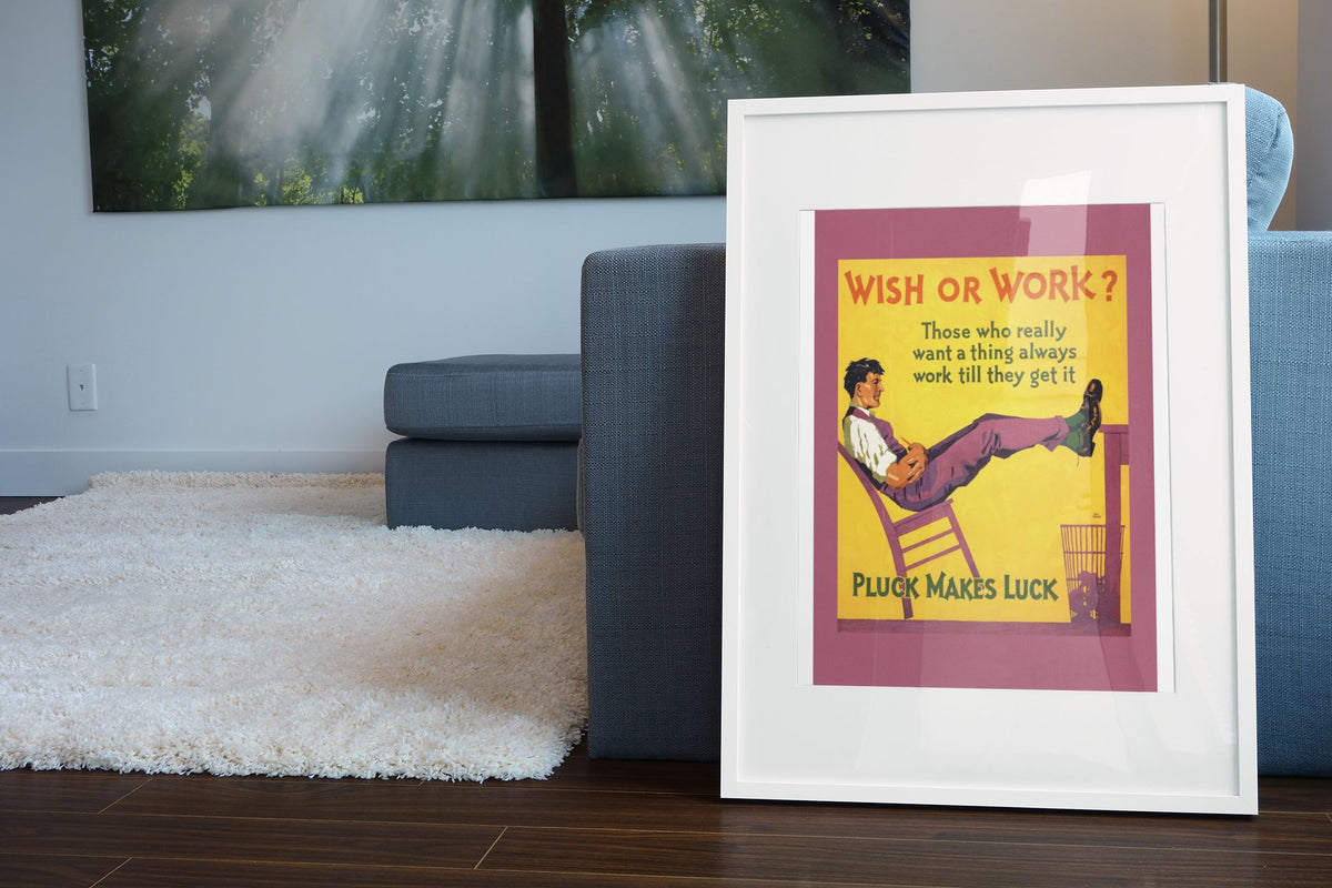 Wish or Work poster in a white frame leaning beside a blue sofa
